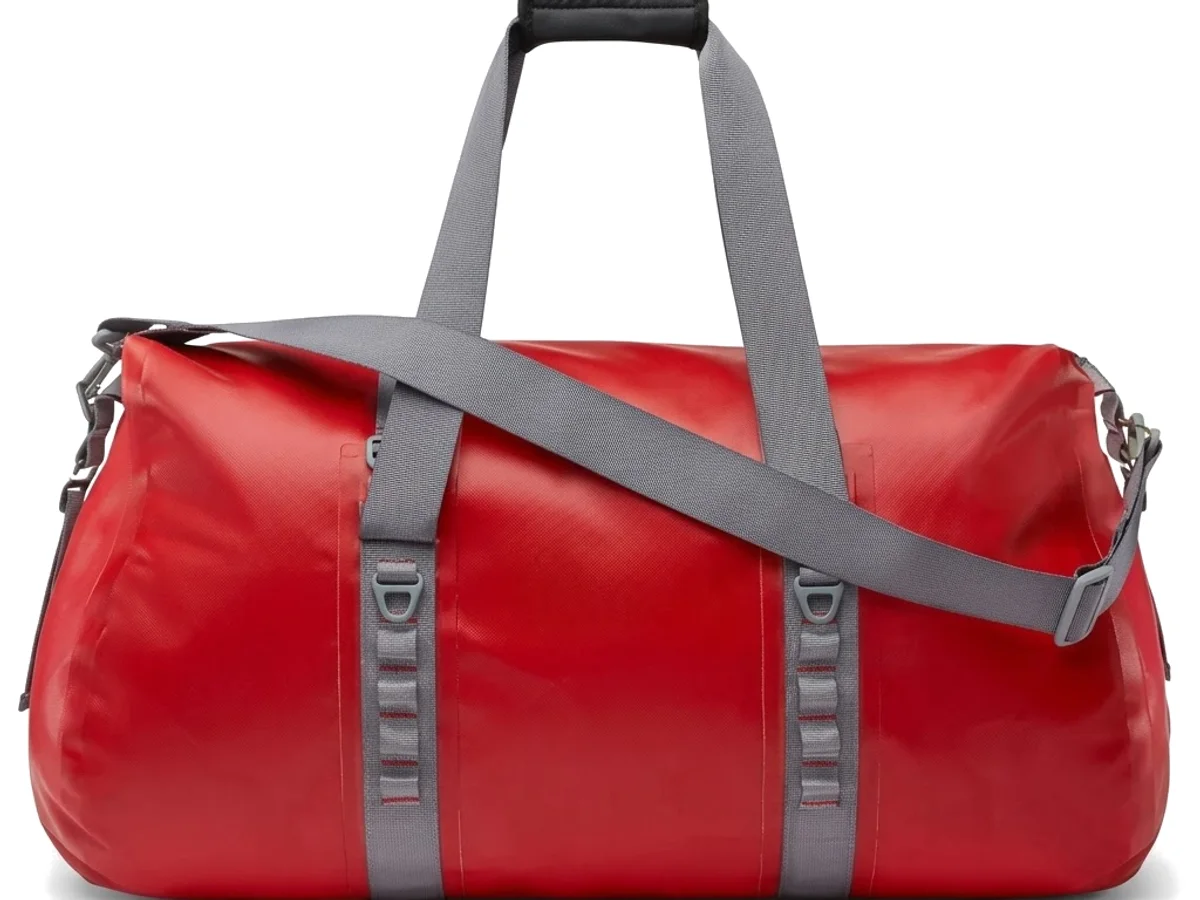 A red coated tarpaulin travel duffel with webbing handles on a plain ground