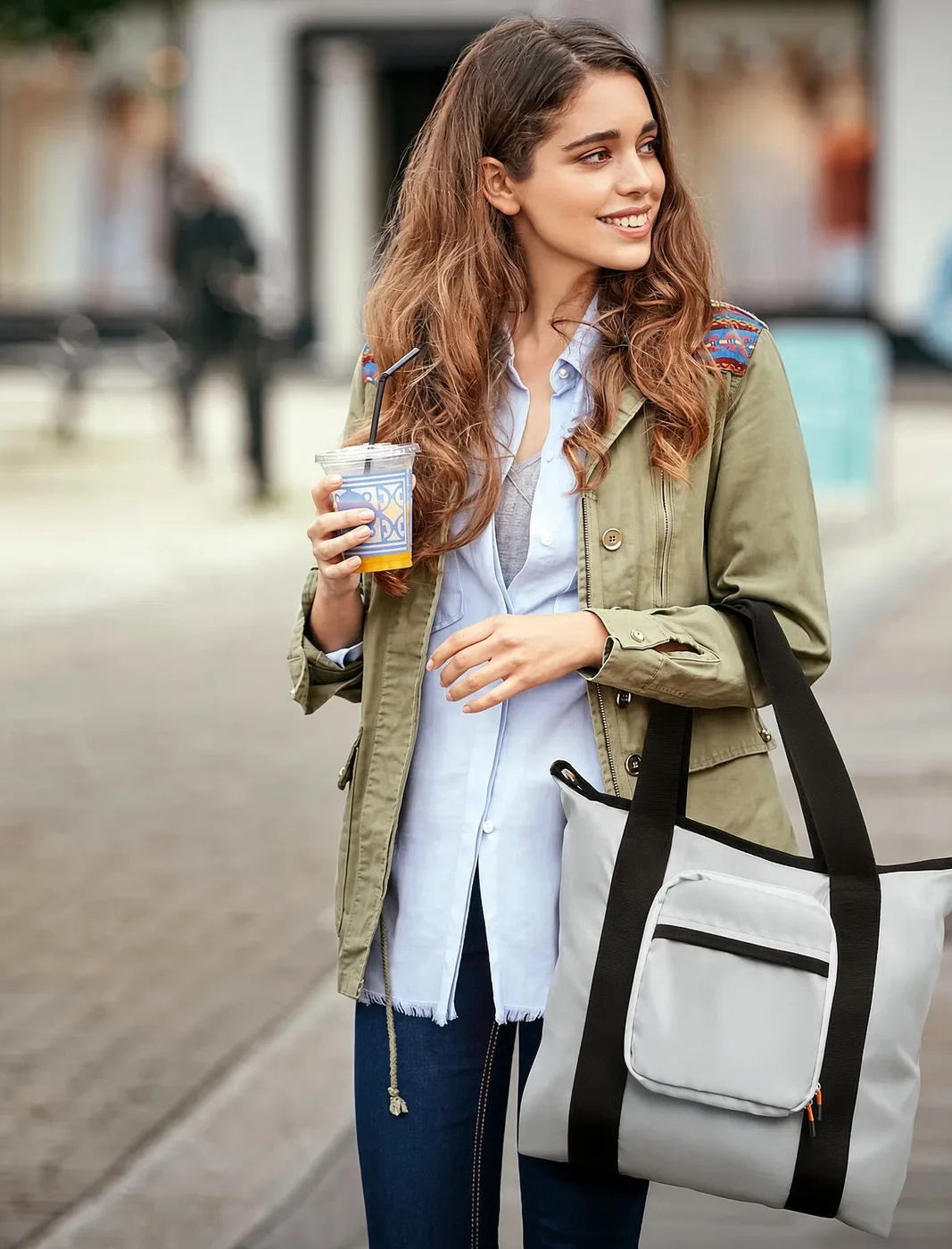 A woman on a city street carrying a white and black tote travel bag